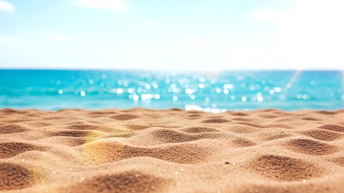 Sunny beach background with golden sand and blurred turquoise ocean water for summer travel concept stock photo