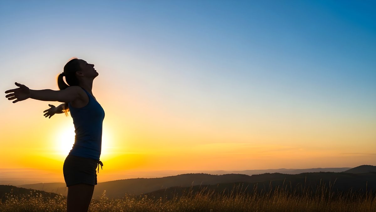 Woman standing with arms outstretched enjoying the sunset view on a mountain peak stock photo
