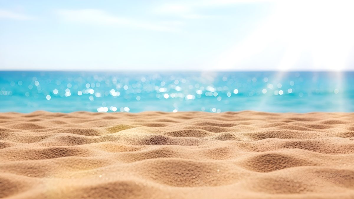 Sunny tropical beach background with golden sand and blurred turquoise ocean water for summer travel stock photo